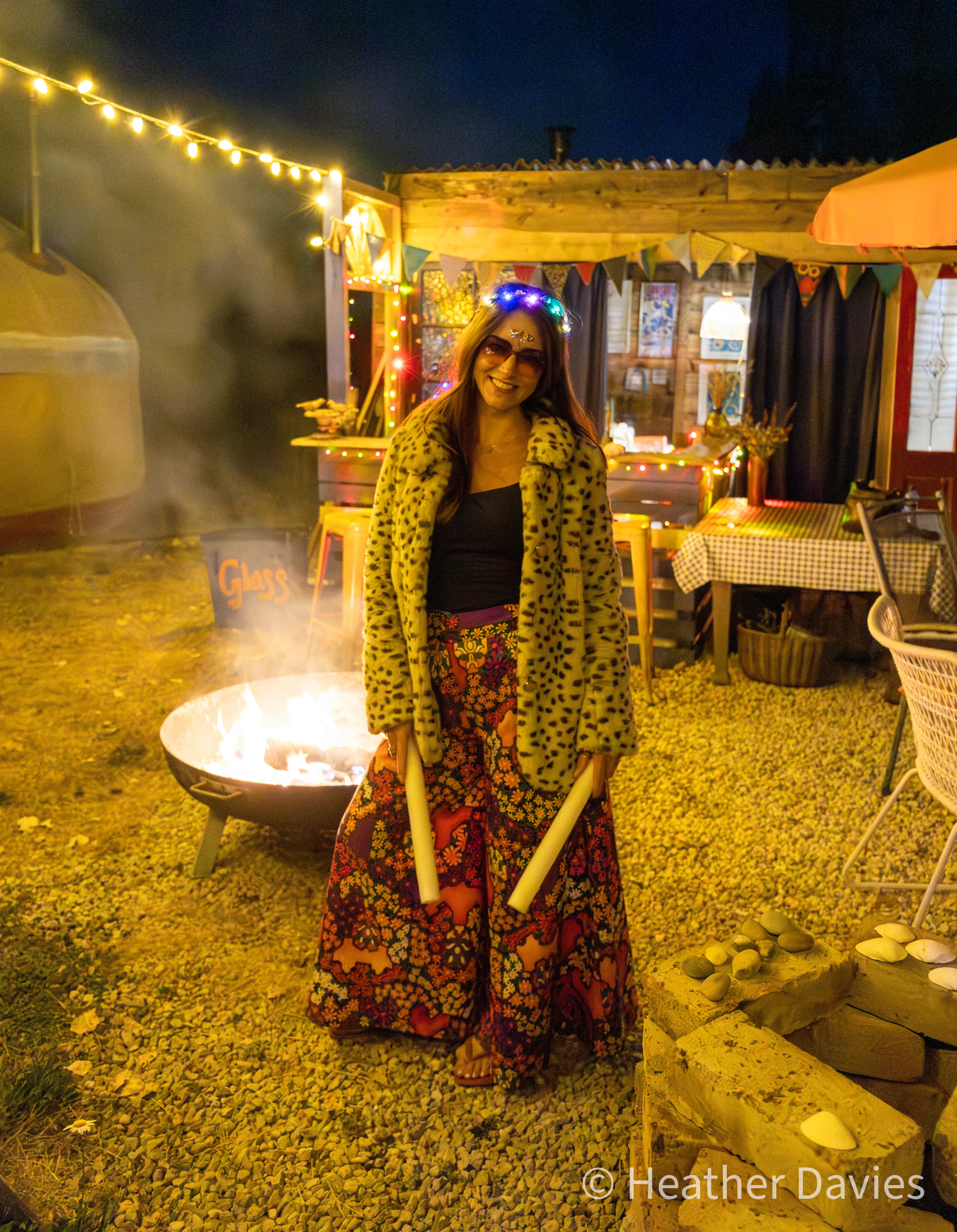 A smiling guest holding glow sticks beside a fire at Bec's 40th birthday celebration