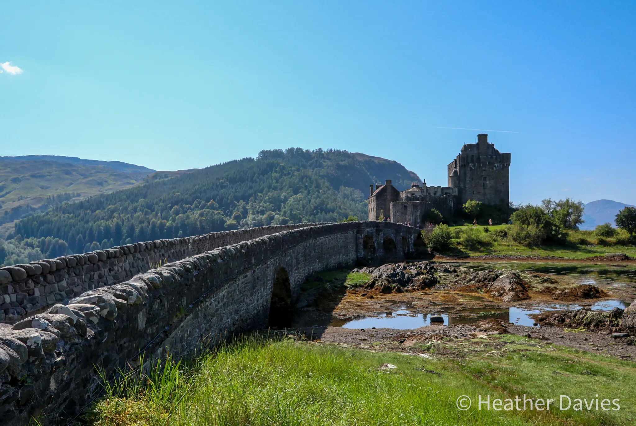 The stone bridge leading to Eilean Donan Castle beside the water on a sunny day